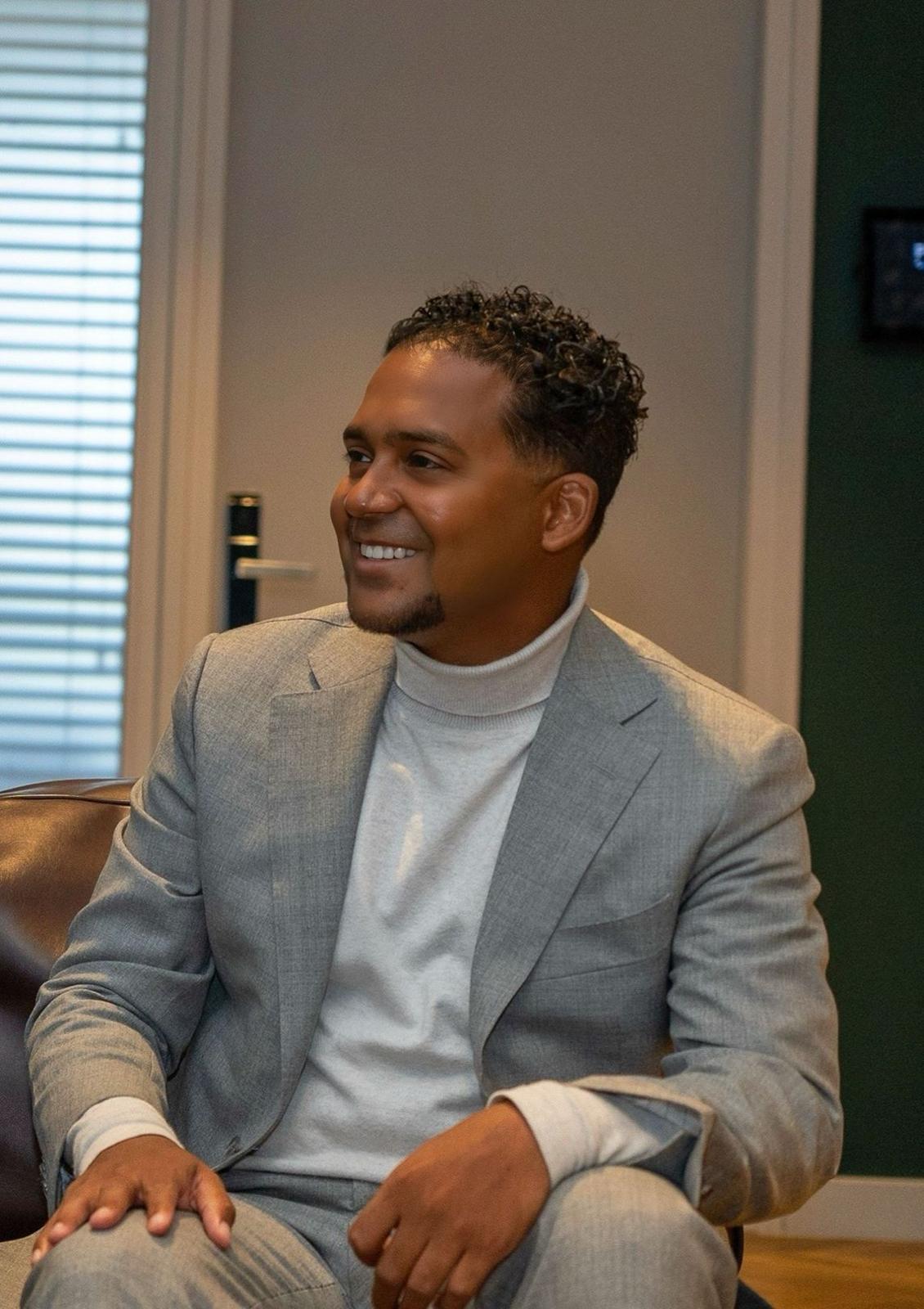 Professional headshot of Sergio Simons Men with shoulder-length blonde hair wearing charcoal blazer and white blouse